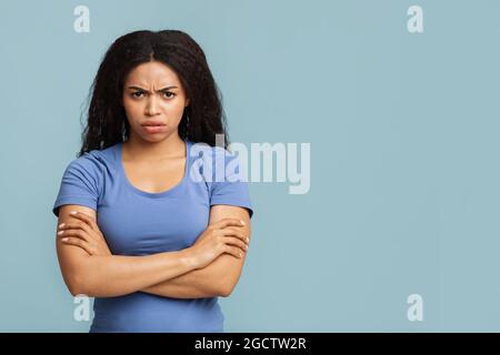 Mürrische Frau. Porträt einer ernsthaften schwarzen Dame, die mit gekreuzten Armen auf blauem Hintergrund mit freiem Platz steht Stockfoto