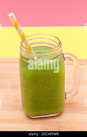 Frischer grüner Smoothie von Apfel, Sellerie und Spinat im gläsernen Smoothie-Glas mit gelbem Cocktailstroh auf Holzschneidebrett. Veganer Detox-Drink. Vegetarische Kultur. Gesunde Ernährung und Obst-Diät Stockfoto