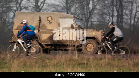 Radfahrer fahren bei der Übung Salisbury Plain, Wiltshire, Großbritannien, vor einem leichten Nutzfahrzeug der britischen Armee des Land Rover Defender vorbei Stockfoto