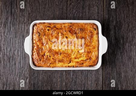 Pikante kartoffelkugel, gebackener Pudding oder Auflauf geriebener Kartoffeln in einer Auflaufform auf einem Holztisch, jüdisches Feiertagsrezept, flaches Lay, Freiraum Stockfoto