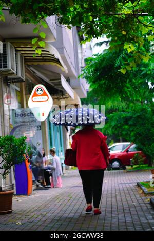 Batumi, Georgien - 30. Juni 2021: Eine Frau mit einem Sonnenschirm läuft auf dem Bürgersteig Stockfoto