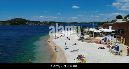 Sibenik, Kroatien - Mai 9.2017: Blick auf weißen Sand Kiesstrand mit Inseln Hintergrund vor blauem Sommerhimmel Stockfoto