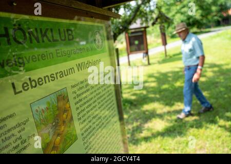 23. Juli 2021, Bayern, Hausen: Gelernter Steinmetz Adam Zentgraf geht an einem Schild mit der Aufschrift 'Wildbienen-Lebensraum' vorbei. Zentgraf begleitet die Besucher durch den Obstgarten-Lehrpfad in Hausen, der Modellgemeinde des UNESCO-Biosphärenreservats Rhön. (Zur dpa-Sommerreihe 'Immaterielles Kulturerbe in Bayern', Korr 'Streuobstwiesen - Vergessene Paradiese?') Foto: Nicolas Armer/dpa Stockfoto