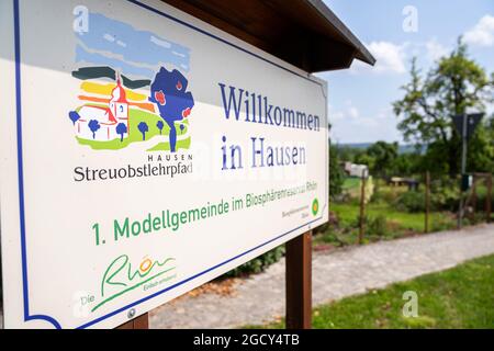 23. Juli 2021, Bayern, Hausen: Vor dem Dorf steht ein Schild mit der Aufschrift "1. Modellgemeinschaft im Biosphärenreservat Rhön". In Hausen, der Modellgemeinde des UNESCO-Biosphärenreservats Rhön, können Besucher durch einen verstreuten Fruchtlehrpfad geführt werden. (Zur dpa-Sommerreihe 'Immaterielles Kulturerbe in Bayern', Korr 'Streuobstwiesen - Vergessene Paradiese?') Foto: Nicolas Armer/dpa Stockfoto