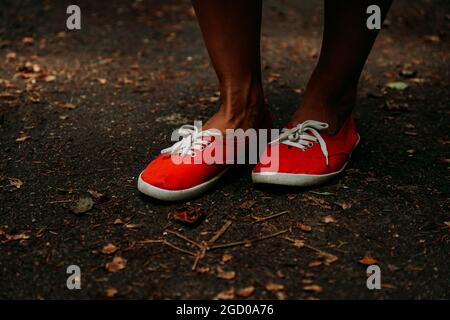 Beine in roten Sneakers auf einem herbstlichen Weg im Park. Schwarze Lederbeine. Sport im Sommerwald Stockfoto