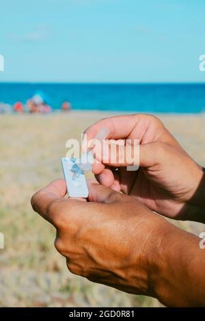 Nahaufnahme eines jungen kaukasischen Mannes am Strand, der seine eigene Probe in das Covid-19-Antigendiagnosetestgerät legte Stockfoto