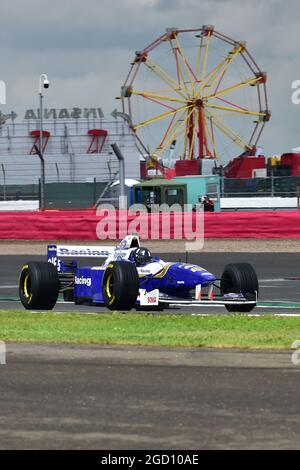 Damon Hill fährt den Williams FW18, in dem er 1996 die F1-Weltmeisterschaft gewann, durch den Loop mit dem großen Rad im Hintergrund. Stockfoto