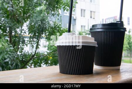 Zwei schwarze Pappbecher mit Deckel im Sommer bei sonnigem Wetter auf einem Holztisch eines Cafés, Cafés oder Restaurants Stockfoto