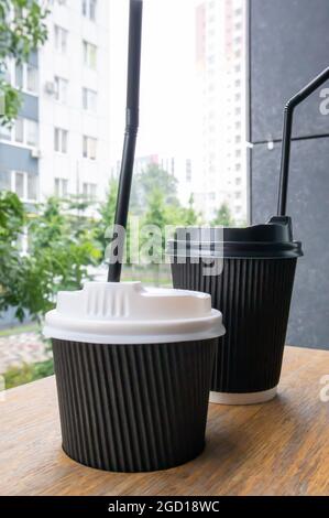 Zwei schwarze Pappbecher mit Deckel im Sommer bei sonnigem Wetter auf einem Holztisch eines Cafés, Cafés oder Restaurants Stockfoto