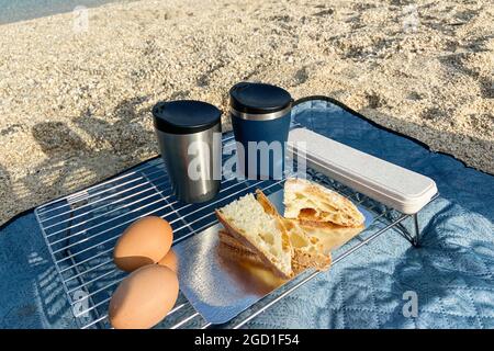 Reiseessen für Outdoor-Aktivitäten. Zwei Metall-Thermobecher, Eier und Toast auf einem Sommerhintergrund. Genießen Sie ein leckeres Essen während der Ausflüge. Stockfoto