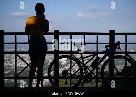 Junge sportliche Frau mit ihrem Fahrrad steht auf einem Bergblick vor einer wunderschönen Landschaft einer fernen Stadt (Chiang Mai) Stockfoto