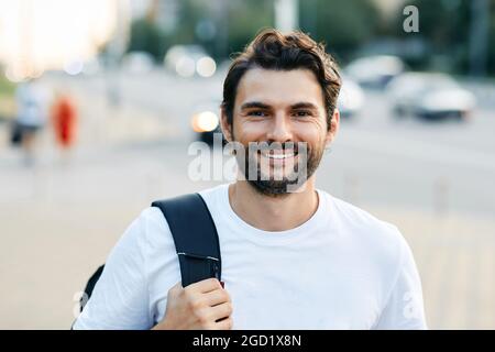 Porträt eines hübschen Mannes mit einem weißen, toothy Lächeln auf einer Stadtstraße mit einem Rucksack Stockfoto