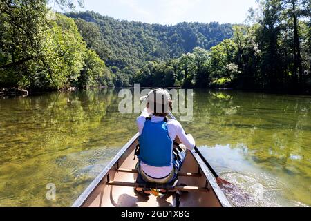 Junge mit Schwimmweste rudert in einem Kanu auf dem Fluss Kolpa, an der Grenze zwischen Slowenien und Kroatien Stockfoto