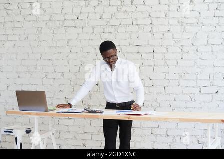 Glücklich fokussierter afroamerikanischer Mann, der einen Videoanruf mit Kundenpartnern führt. Der junge schwarze Mann nutzt im modernen Büro einen Laptop. Stockfoto