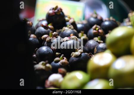 Nachtmarkt in Thailand: Eine Menge Mangostan und Zitrusfrüchte auf einem Stall unter hellem elektrischem Licht Stockfoto