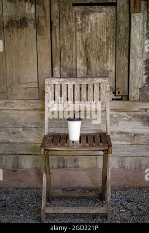 Vertikale Aufnahme einer weißen eisgekühlten Kaffeetasse auf einem antiken Holzstuhl Stockfoto