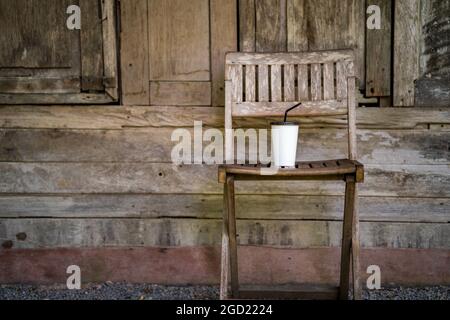 Weiße eisgekühlte Kaffeetasse auf einem antiken Holzstuhl Stockfoto