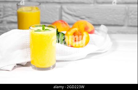 Smoothie mit Pfirsich und Minzblatt mit Stück Tuch auf weißem Backstein Hintergrund, horizontale Auflösung, gesunde Sommerdiät Stockfoto