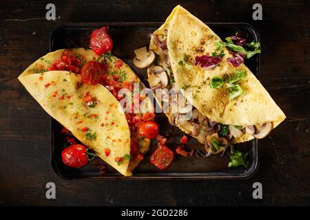 Blick von oben auf leckere hausgemachte Omelettes mit Pilzen und Tomaten auf Tablett auf Holztisch serviert Stockfoto