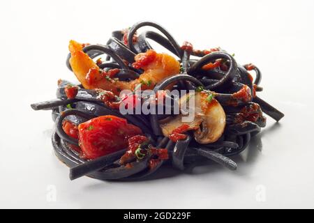 Nahaufnahme Haufen schwarzer Spaghetti mit Garnelen und gebratenem Gemüse auf weißem Hintergrund serviert Stockfoto