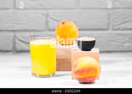 Kreatives Stillleben mit Frucht-Smoothie, Pfirsich und Maca auf Holzpodien auf weißem Backstein-Hintergrund, horizontal, Copy Space, Trendy Food Stockfoto