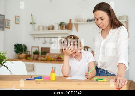 Junges Mädchen macht Hausaufgaben während außerschulischen Klassen mit einem Tutor. Frustrierte junge Mutter oder Tutorin, die zu Hause Kinder unterrichtet, Fernschulbildung Stockfoto