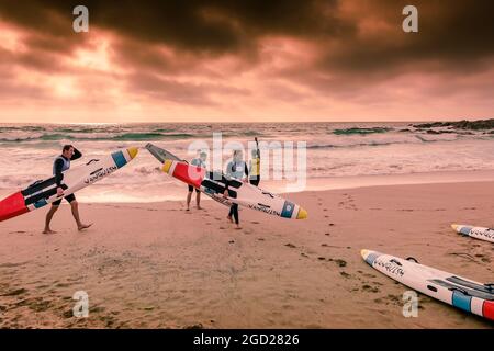 Am späten Abend können Mitglieder des Newquay Surf Lifesaving Club bei einer Trainingseinheit am Fistral Beach in Newquay in Cornwall beleuchtet werden. Stockfoto