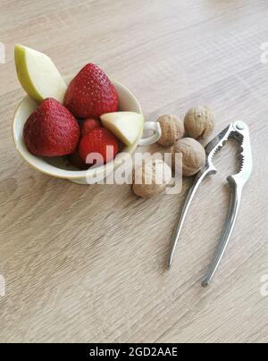 Frische Erdbeeren, Apfelstücke, Walnüsse und ein Nussknacker Stockfoto