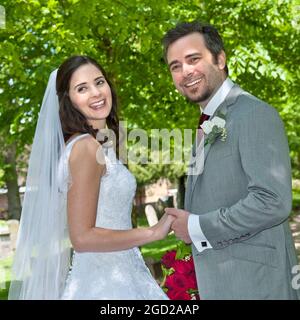 BRAUT BRÄUTIGAM KIRCHPFAD HEIRATETE TRADITIONELLE WEISSE HOCHZEIT GLÜCKLICHE attraktive junge traditionelle Braut und Bräutigam haben gerade geheiratet, die einen von Bäumen gesäumten Pfad entlang gehen Stockfoto