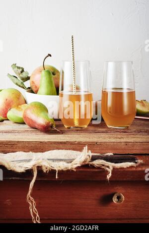 Zwei Gläser Fruchtgetränk, frische Äpfel und Birnen auf einem Holztisch. Stockfoto