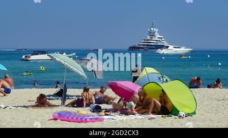St. Tropez (Plage de pampelonne), Frankreich - Juni 9. 2016: Blick auf Menschen, die sich am Sandstrand entspannen, Mittelmeer mit Yachten Hintergrund (Fokus auf niedrig Stockfoto