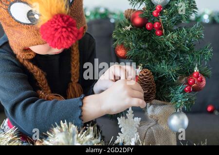 Weihnachten und Neujahr Vorbereitung Konzept. Kind schmückt Weihnachtsbaum mit Kugeln und Schneeflocken in Kleid und weihnachtsmütze. Tannenbaum A Stockfoto