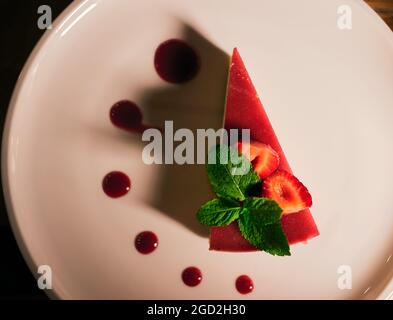 Käsekuchen auf einer weißen Keramikplatte, garniert mit frischen Erdbeeren und Erdbeersirup. Stockfoto