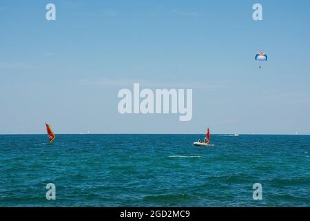 Menschen Windsurfen vor der Adriaküste im Juli nördlich von Novigrad, Istrien, Kroatien. Im Hintergrund ist ein Parasailer oder Parascender Stockfoto