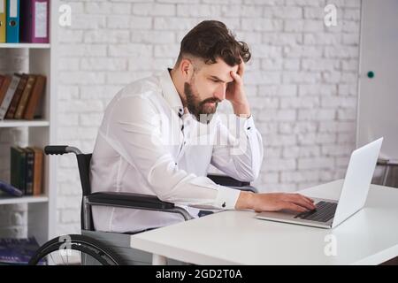 Geschäftsmann, der im Rollstuhl sitzt und mit einem Laptop arbeitet Stockfoto