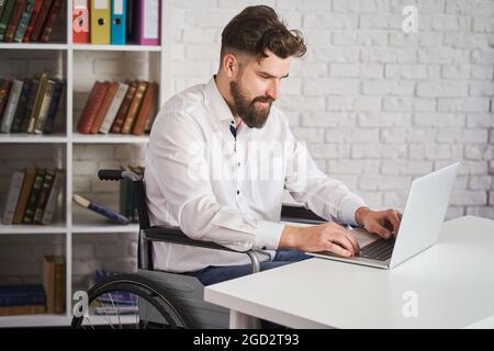 Der Chef sitzt im Rollstuhl und arbeitet an einem Laptop Stockfoto