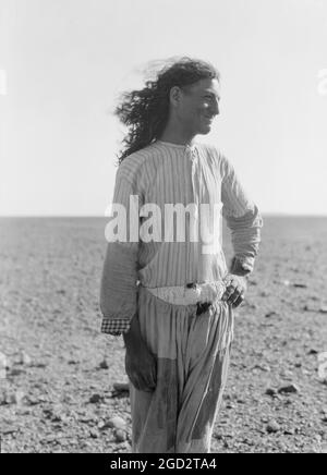 Beduinenleben in Trans-Jordanien, ein beduinenstraßenbulder mit langen Haaren in Trans-Jordanien ca. 1920 Stockfoto