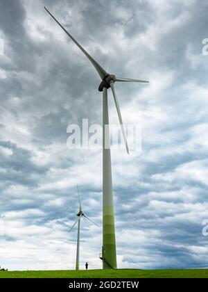 Kontrastieren Sie riesige Windturbinen und einen Jungen am Fuß eines Pfahls. Erneuerbare Energien und nachhaltige Ressourcen, Windmühlen Stockfoto