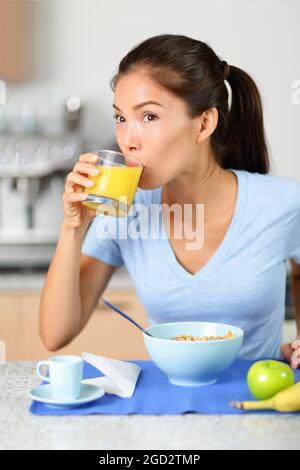 Frühstück zu Hause Asiatin trinkt frische kalt gepresste Orangensaft Getränk während der Getreidemahlzeit in der Küche. Vertikales Hochformat. Stockfoto