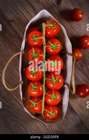 Draufsicht auf Traversen von kleinen reifen Kirschtomaten im Beutel auf Holzhintergrund Stockfoto