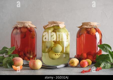 Drei hausgemachte Dosenfrüchte, Apfel- und Kirschkompott in großen Gläsern auf einem grauen Tisch. Stockfoto