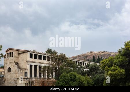 Stoa of Attalos im Grünen, Architektur des alten Stadtzentrums von Athen am grauen Tag mit epischen Wolken und Blick auf den Akropolis-Hügel Stockfoto