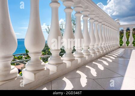 Traditionelle weiße Baluster aus der Nähe. Griechische Architektur Elemente der Terrasse. Blick durch den Balkon auf die klare blaue Küste der Ägäis. Sommerurlaub auf dem Land Stockfoto