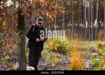 Ein Mann im Wald, ein Jäger, ein Pilzsammler in einer Militärmütze schaut nach unten und hält eine Zigarette. Wanderer im Wald. Landschaft im Wald. Ansicht von Stockfoto