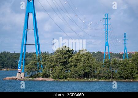 Helsinki / Finnland - 10. AUGUST 2021: Eine Reihe moderner Hochspannungsmasten am Ufer gegen den bewölkten Himmel. Stockfoto