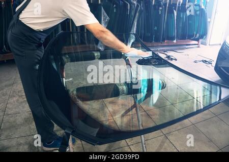 Glasurarbeiter entfettet Glasscheibe oder Windschutzscheibe vor der Montage auf dem Auto in der Werkstatt. Stockfoto