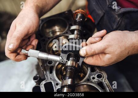 Ein Messgerät in der Hand misst die Nockenwelle vor dem Hintergrund eines Motors in geringer Schärfentiefe Stockfoto