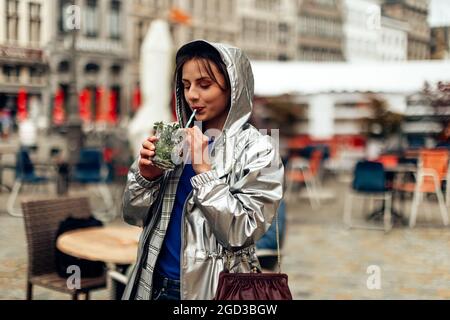 Junges Weibchen im Regenmantel, das mit dem Stroh trinkt Stockfoto