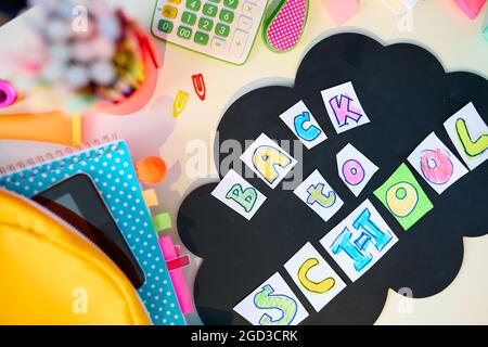 Zurück zur Schule. Blick von oben auf den weißen Schreibtisch mit Arbeitsbüchern, Schreibwaren, Wolke und Aufschrift für den Rücken zur Schule im Studentenzimmer an sonnigen Tagen. Stockfoto