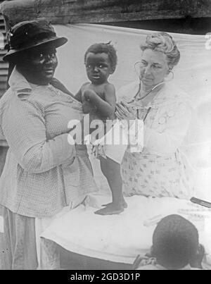 Eine afroamerikanische Frau lässt ihr Kleinkind etwa zwischen 1918 und 1928 von einem Arzt oder einer Krankenschwester untersuchen Stockfoto